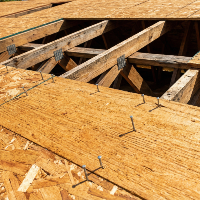 Close-up of OSB roof decking being installed over wooden trusses with exposed nails and metal truss plates during a roof replacement
